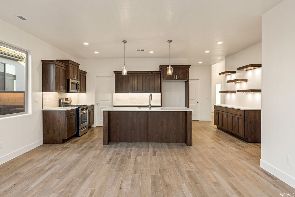 Kitchen with light wood-type flooring, a center island with sink, and stainless steel appliances