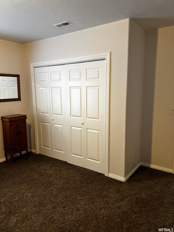 Unfurnished bedroom with dark carpet, a textured ceiling, and a closet