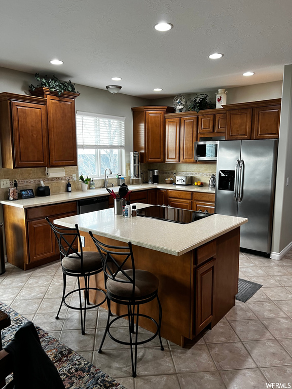 Kitchen featuring black appliances, a center island, tasteful backsplash, and light tile floors