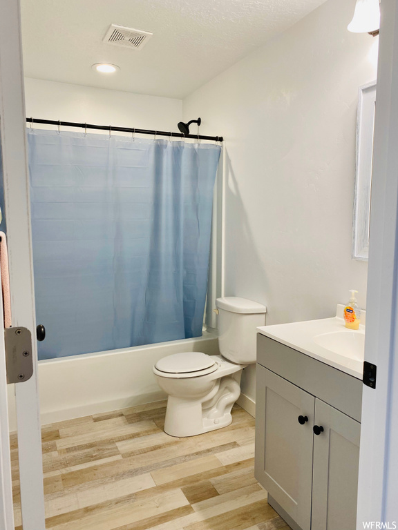 Full bathroom with vanity, shower / tub combo with curtain, hardwood / wood-style flooring, toilet, and a textured ceiling