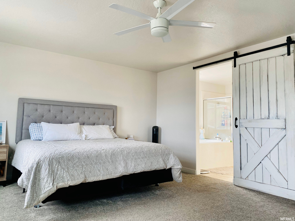 Carpeted bedroom featuring ensuite bathroom, a barn door, and ceiling fan