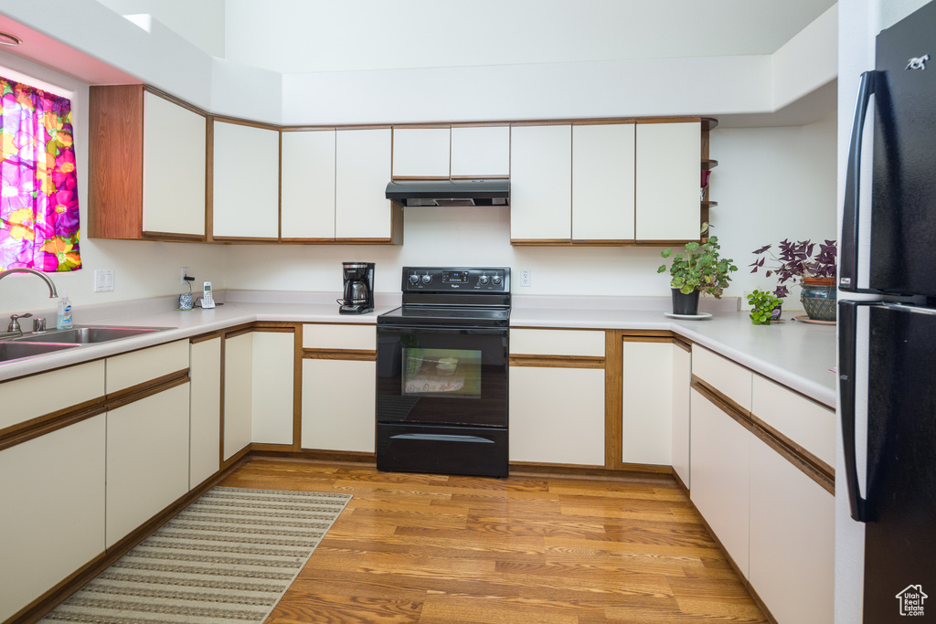 Kitchen with white cabinets, light hardwood / wood-style floors, sink, and black appliances