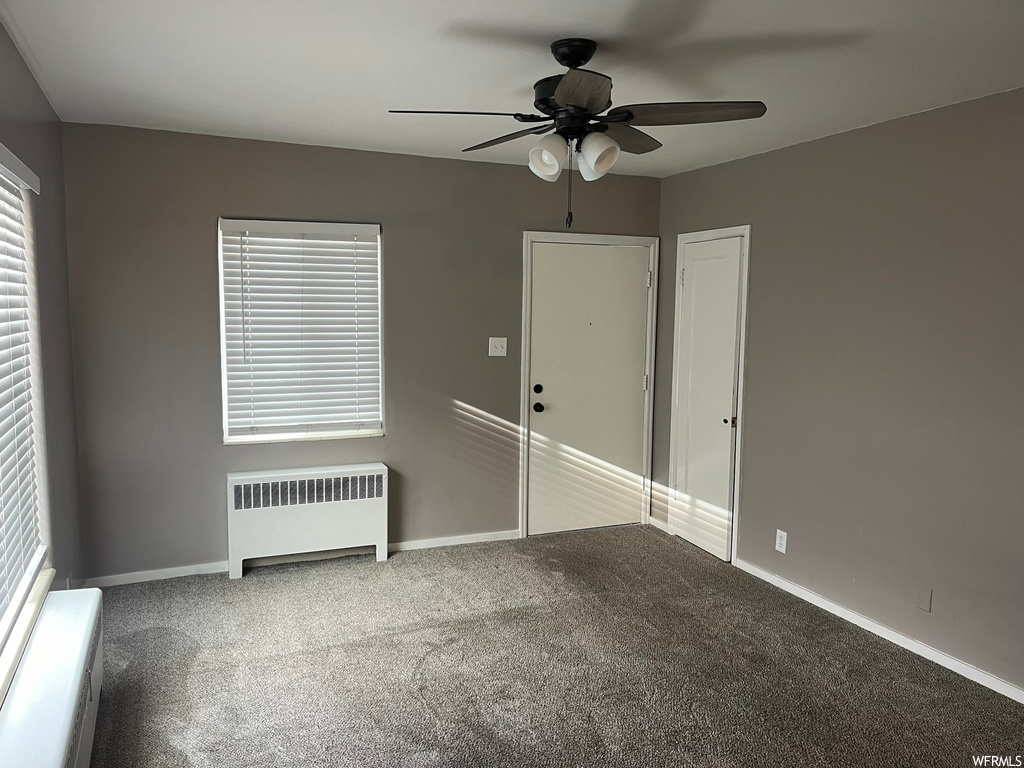 Carpeted spare room with ceiling fan, a wealth of natural light, and radiator heating unit