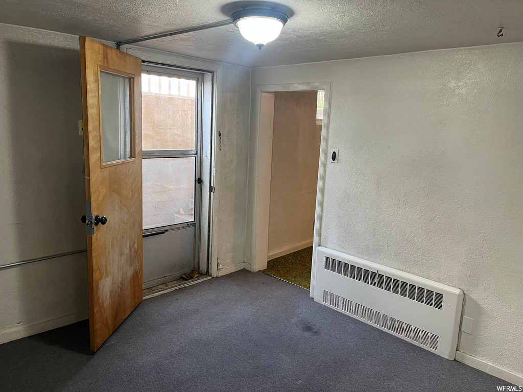 Empty room with dark colored carpet, a textured ceiling, and radiator heating unit