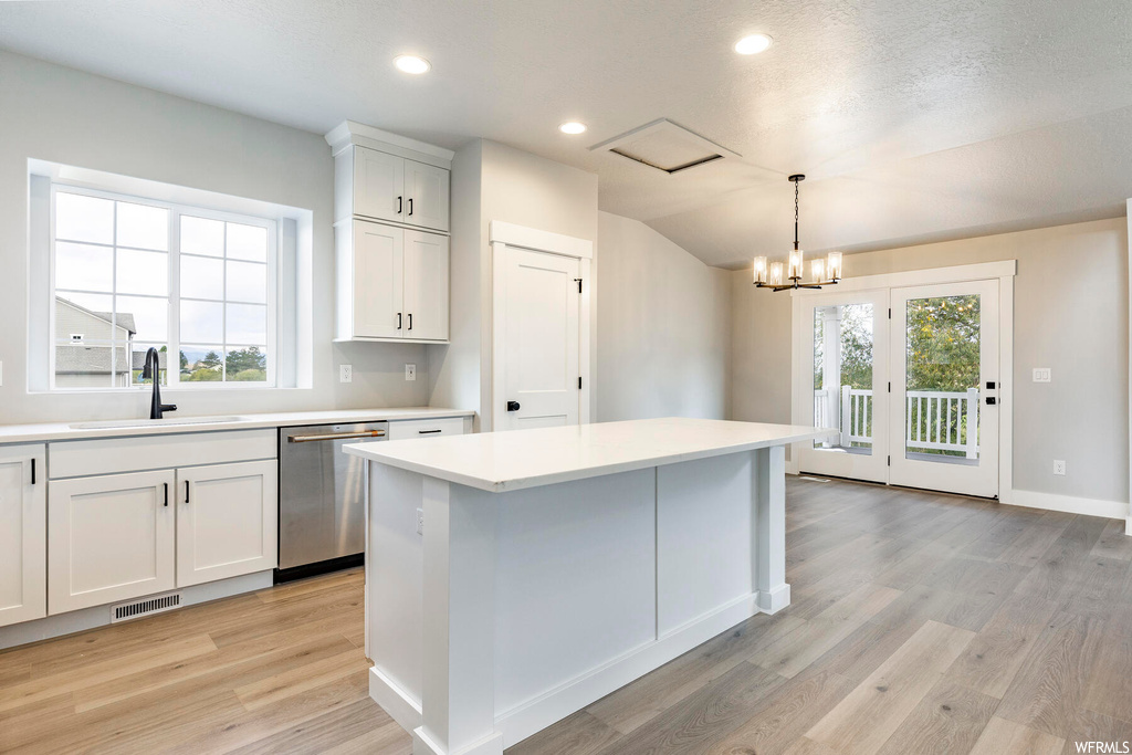 Kitchen featuring an inviting chandelier, light hardwood / wood-style floors, stainless steel dishwasher, white cabinets, and sink
