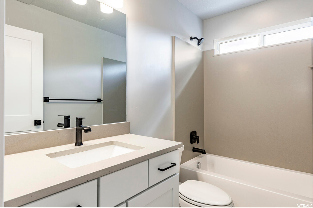 Full bathroom with toilet, vanity with extensive cabinet space, and washtub / shower combination