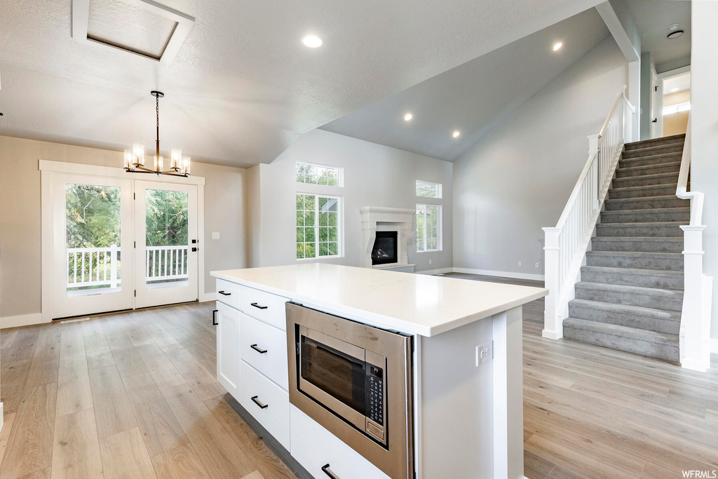 Kitchen featuring a chandelier, a kitchen island, light wood-type flooring, stainless steel microwave, and white cabinetry