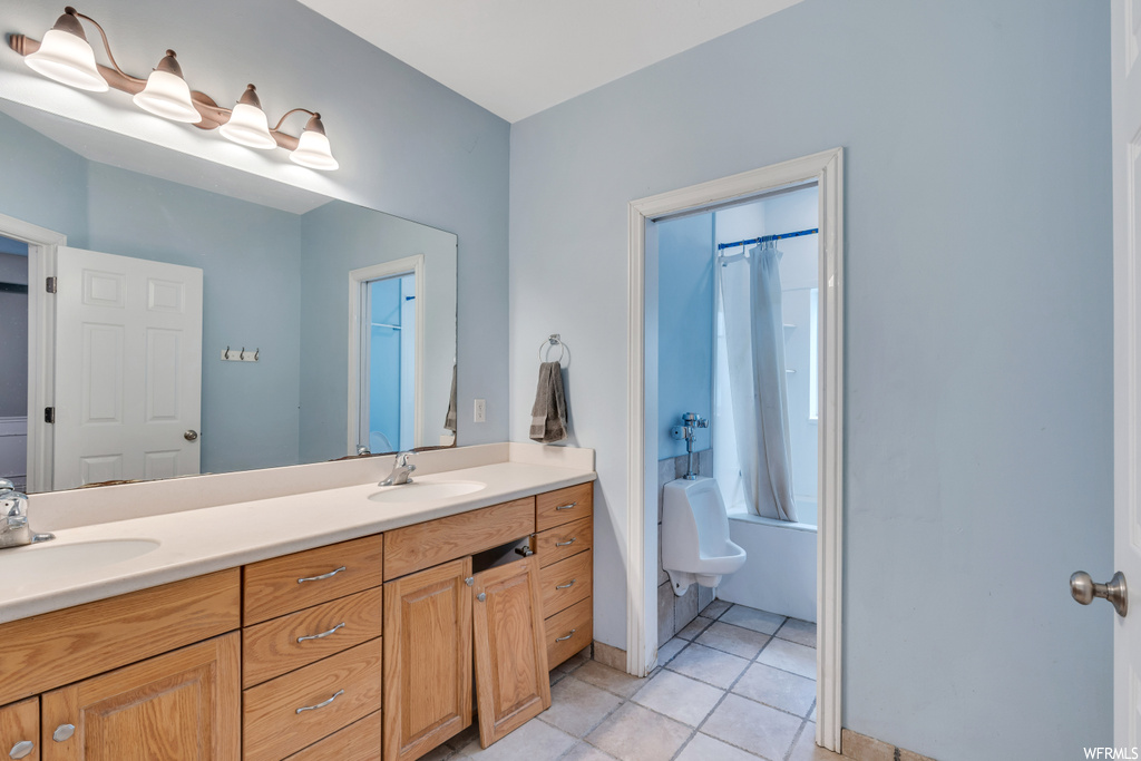 Bathroom featuring dual sinks, vanity with extensive cabinet space, and tile flooring