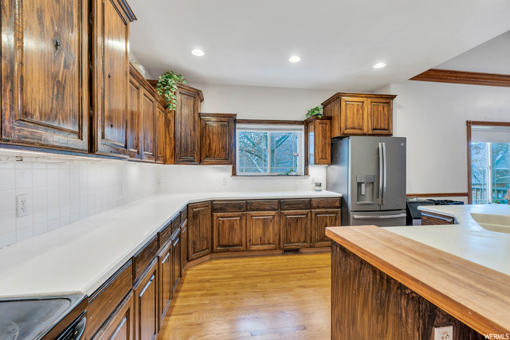 Kitchen with ornamental molding, light hardwood / wood-style flooring, stainless steel fridge with ice dispenser, and tasteful backsplash