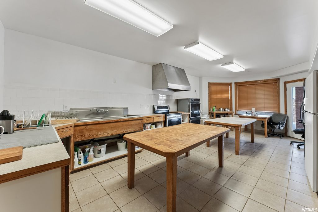 Kitchen featuring stainless steel appliances, light tile floors, wall chimney range hood, and backsplash
