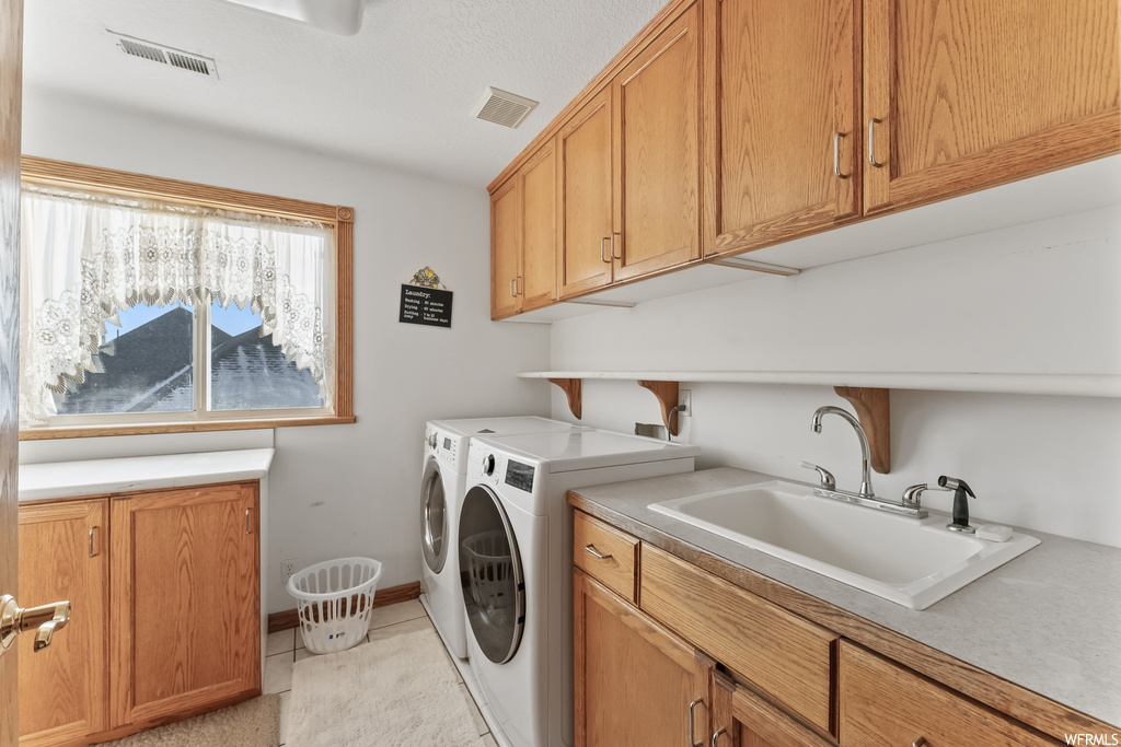 Laundry room with sink, cabinets, washer and clothes dryer, and light tile floors