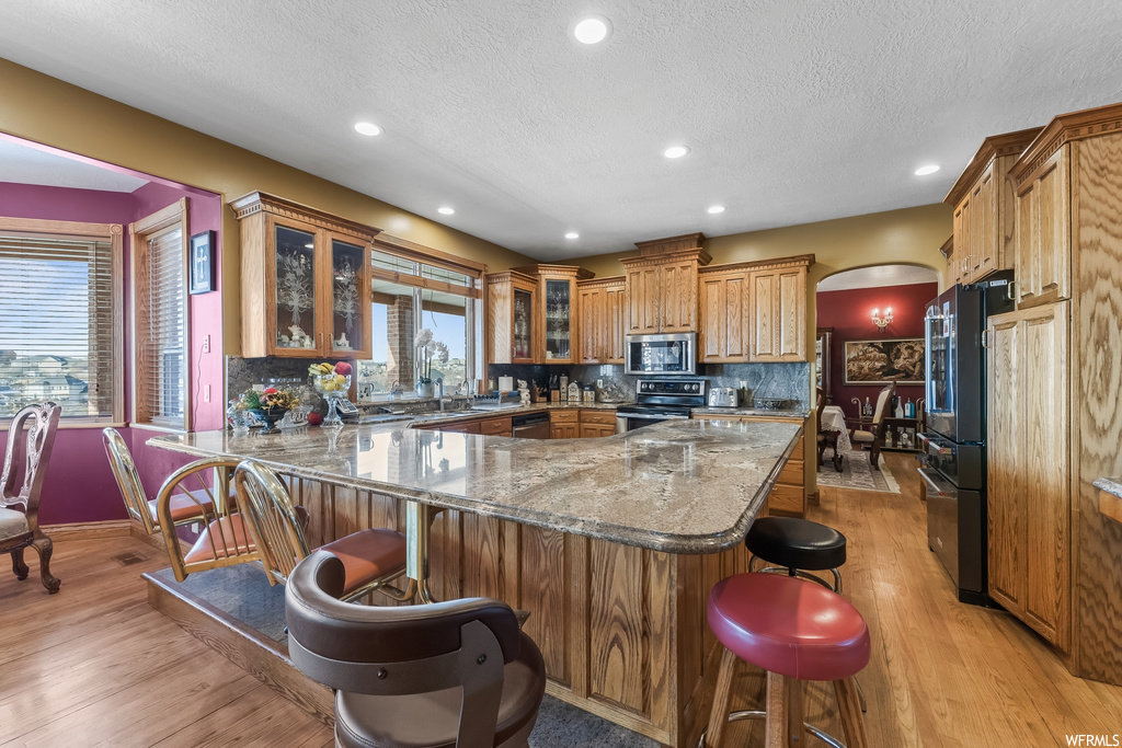Kitchen featuring light hardwood / wood-style floors, tasteful backsplash, light stone counters, a kitchen bar, and electric range