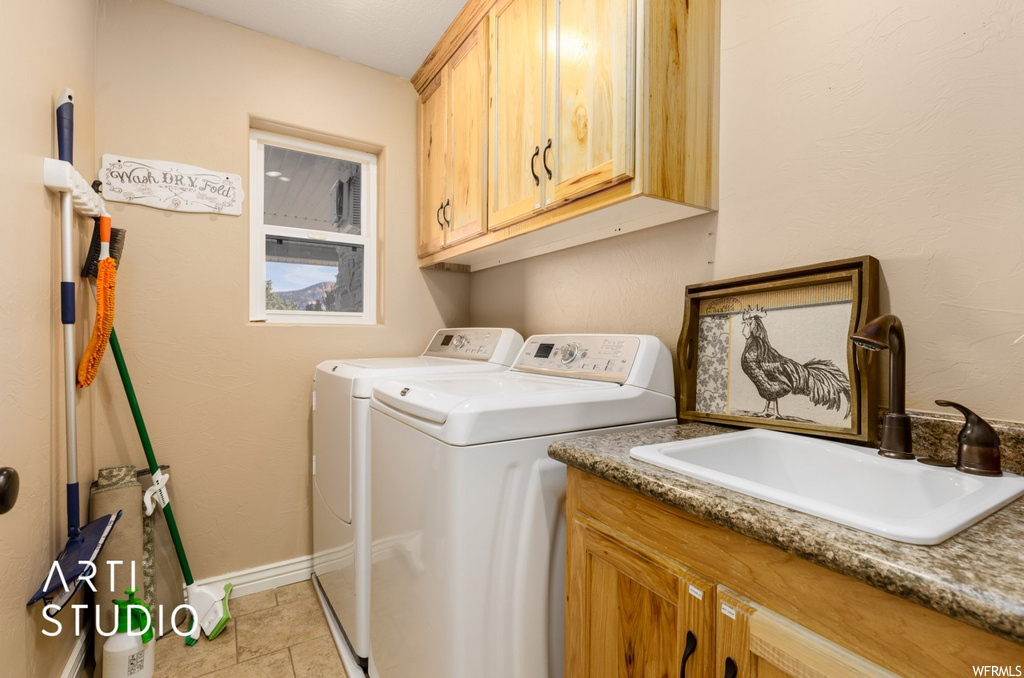 Washroom featuring washing machine and clothes dryer, cabinets, sink, and light tile floors