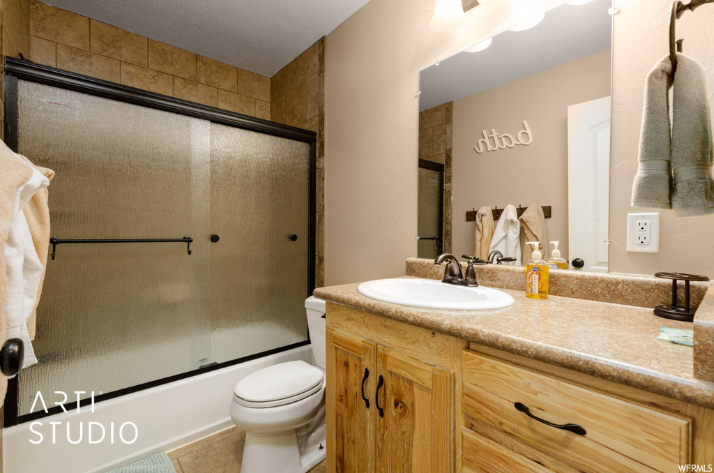 Full bathroom featuring tile floors, oversized vanity, toilet, and enclosed tub / shower combo