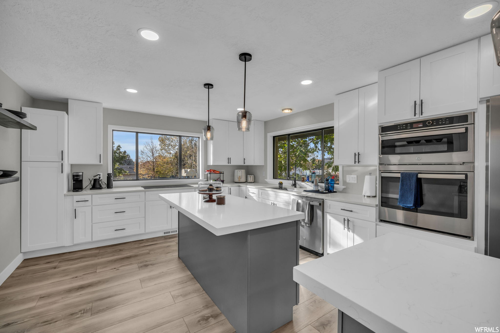 Kitchen featuring stainless steel appliances, white cabinets, pendant lighting, and a center island