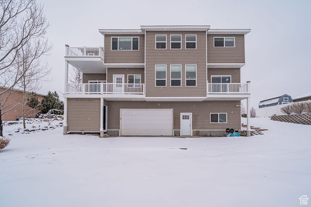 Snow covered rear of property with a garage and a balcony