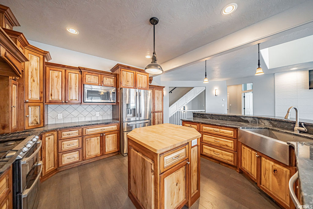 Kitchen with decorative light fixtures, appliances with stainless steel finishes, a center island, sink, and dark wood-type flooring