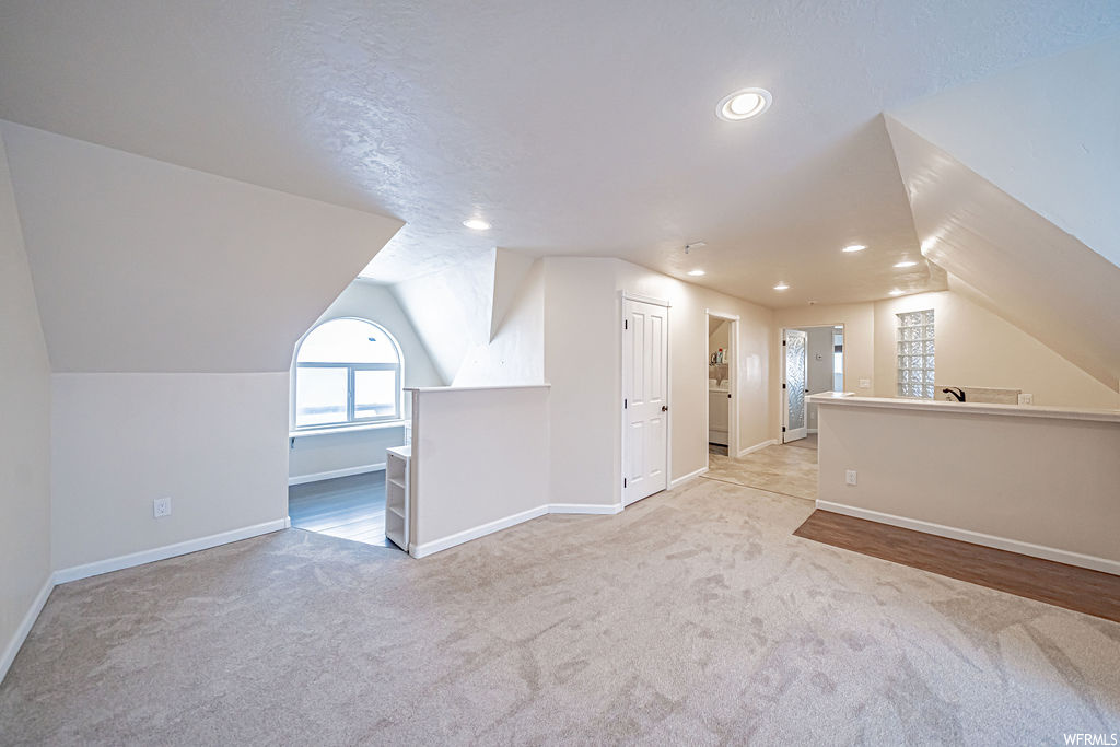 Bonus room with lofted ceiling, a textured ceiling, and light colored carpet