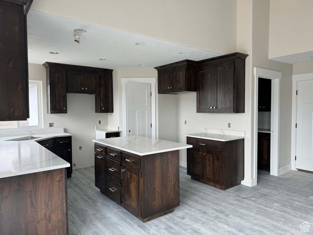 Kitchen featuring a kitchen island, dark brown cabinets, light stone counters, and light hardwood / wood-style flooring