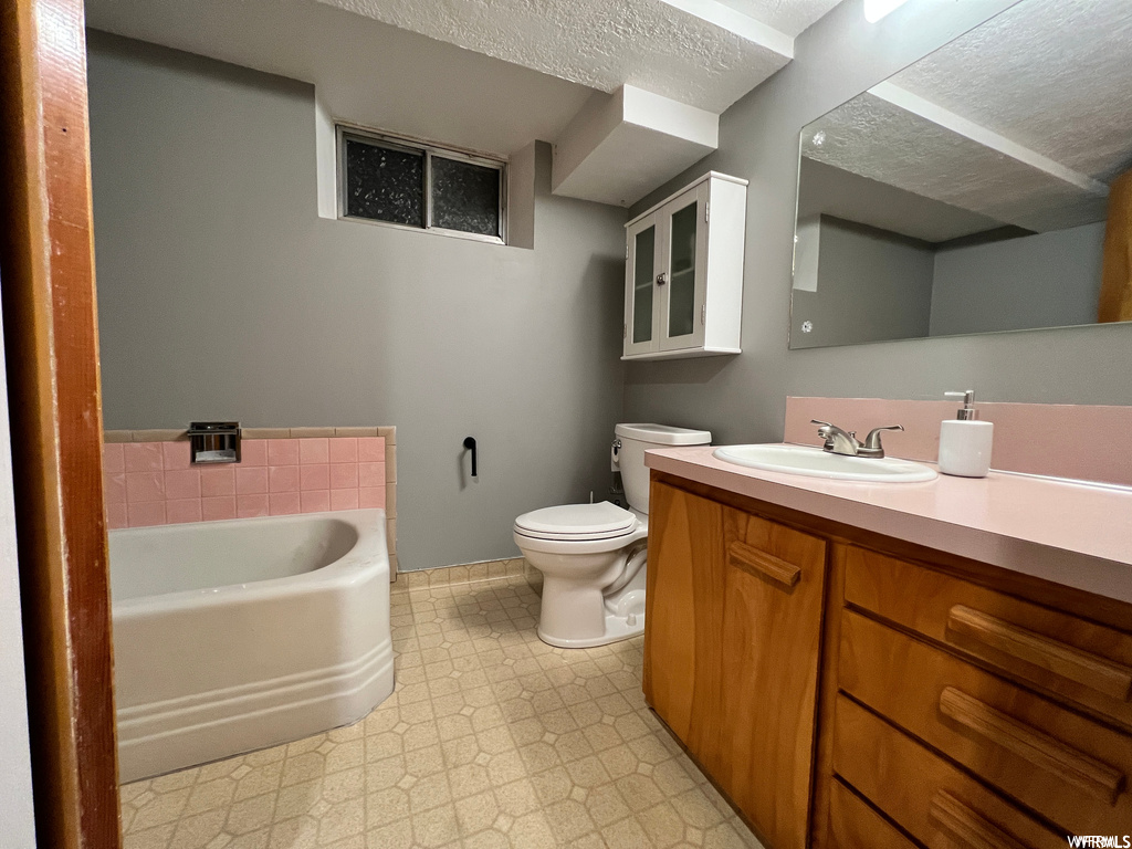 Bathroom with toilet, a washtub, vanity with extensive cabinet space, tile flooring, and a textured ceiling
