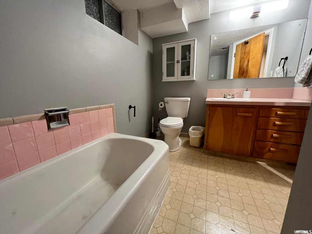Bathroom with toilet, vanity with extensive cabinet space, a tub, and tile flooring