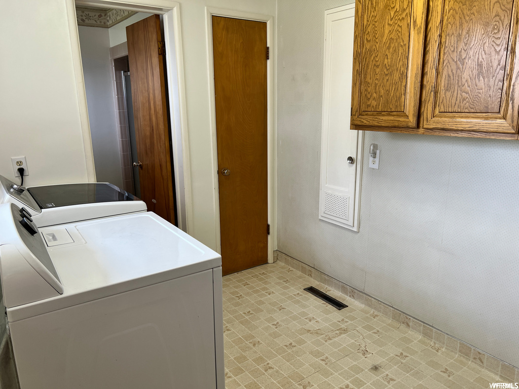 Clothes washing area with separate washer and dryer, cabinets, and light tile floors