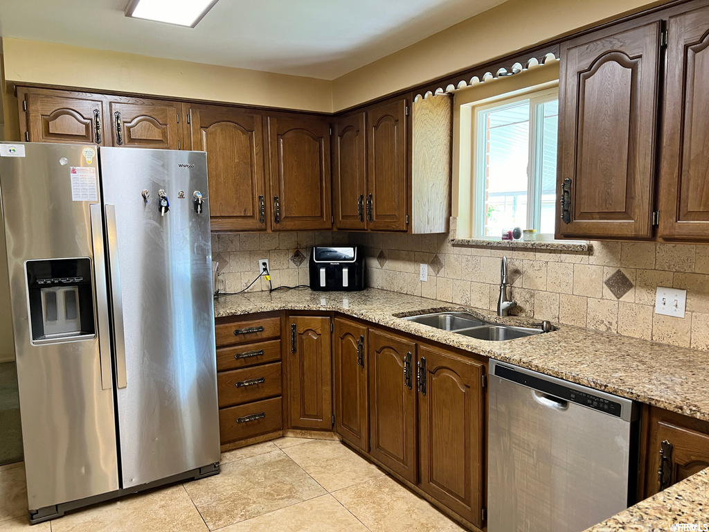 Kitchen with light tile floors, tasteful backsplash, light stone countertops, sink, and stainless steel appliances