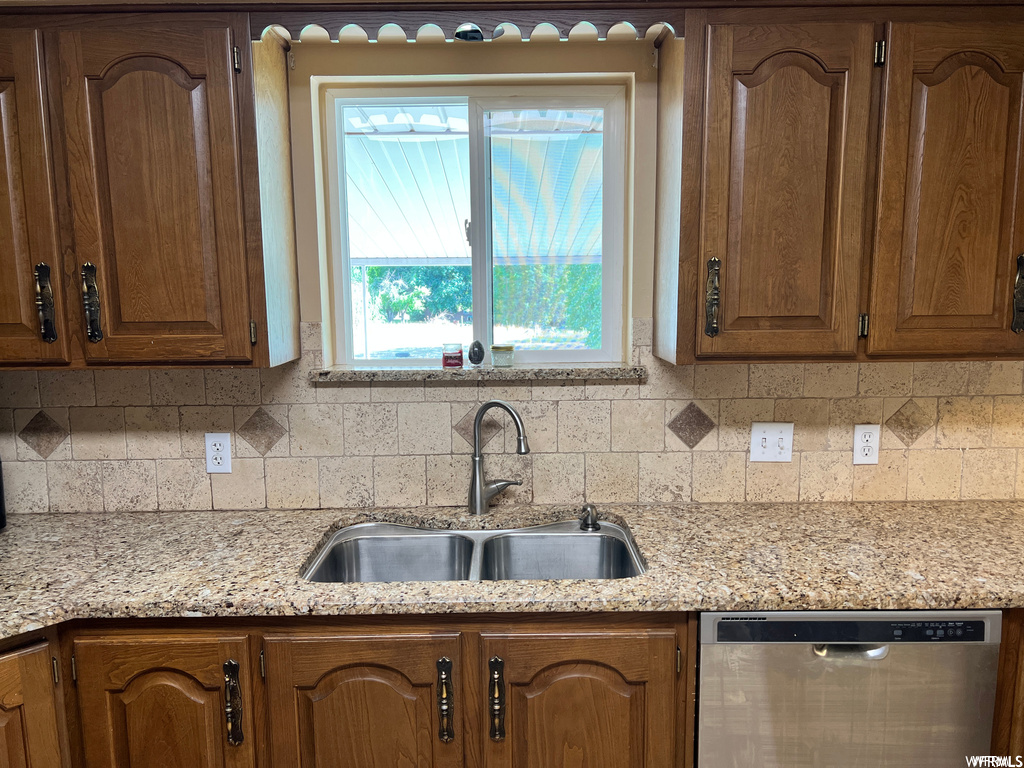 Kitchen with sink, dishwasher, light stone countertops, and backsplash