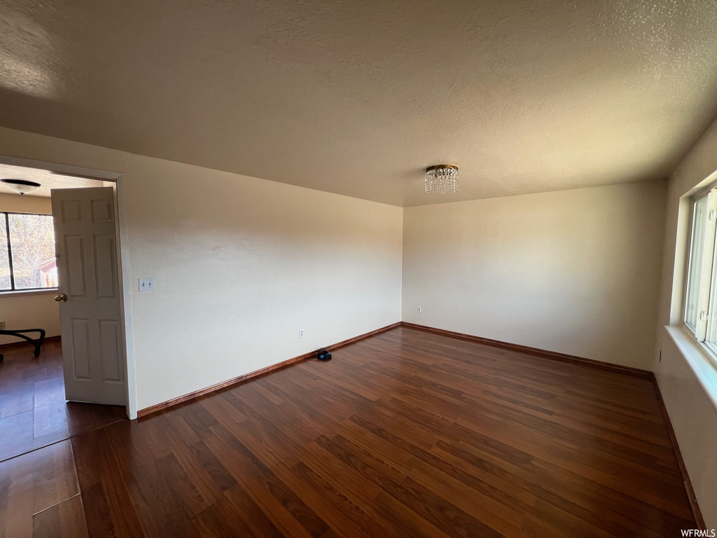 Empty room with a textured ceiling and dark hardwood / wood-style floors