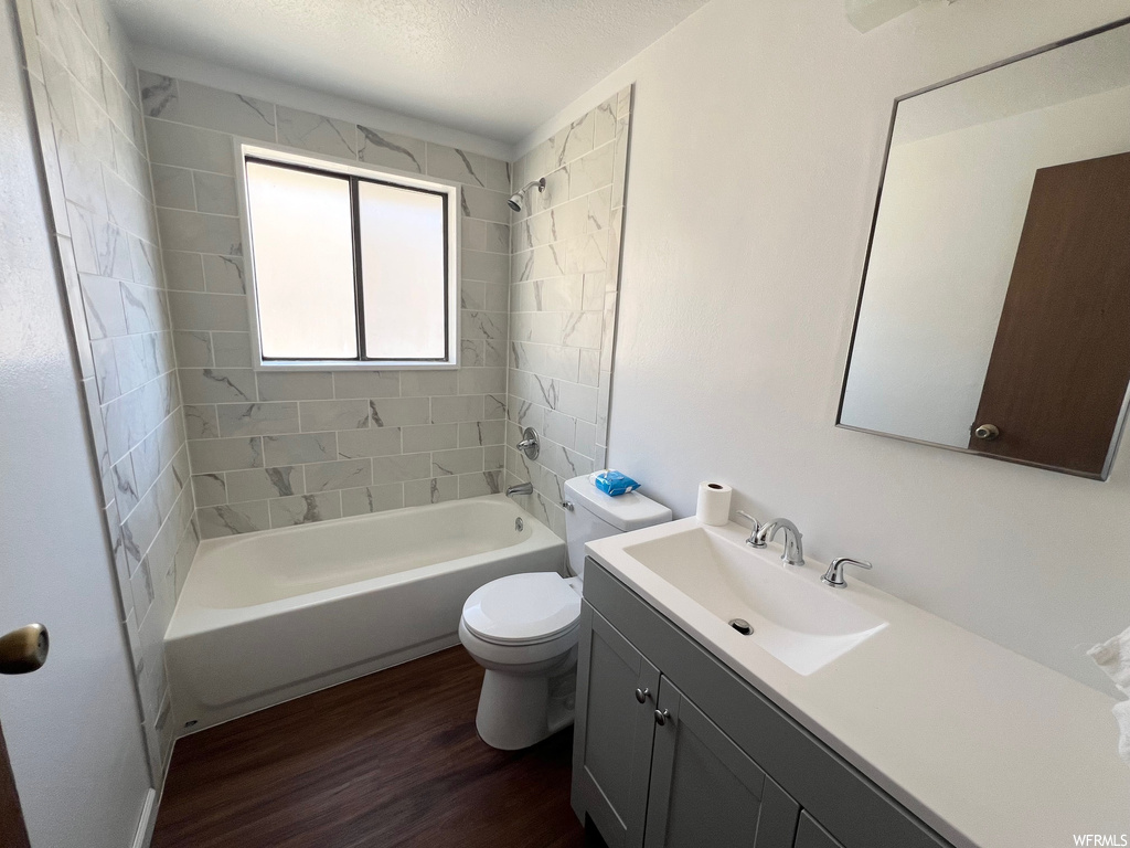 Full bathroom with tiled shower / bath, toilet, vanity with extensive cabinet space, and hardwood / wood-style flooring