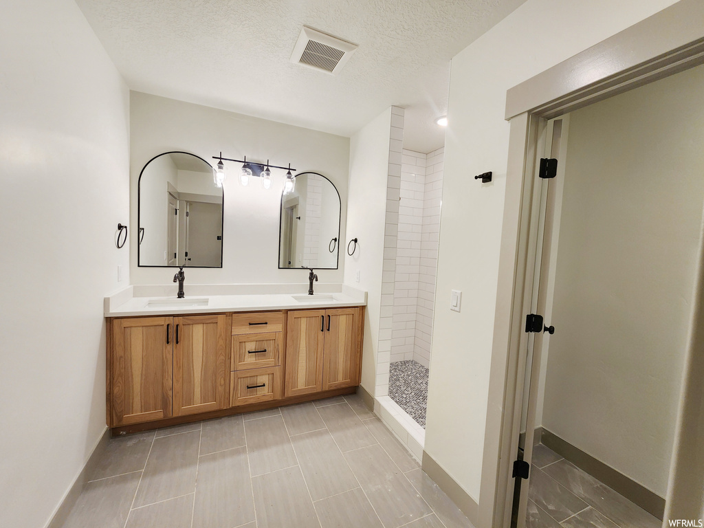 Bathroom with tile flooring, a textured ceiling, double sink vanity, and tiled shower
