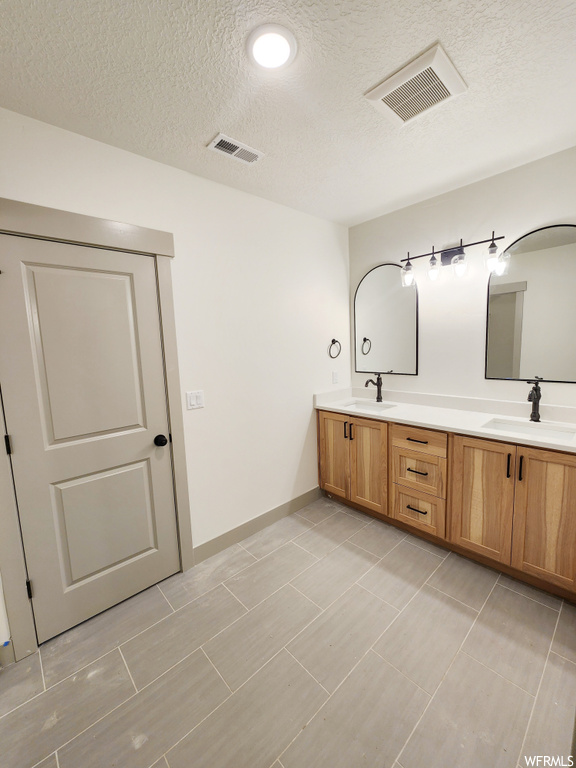 Bathroom with large vanity, a textured ceiling, tile flooring, and dual sinks