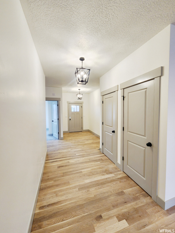 Hall featuring an inviting chandelier, a textured ceiling, and light hardwood / wood-style flooring