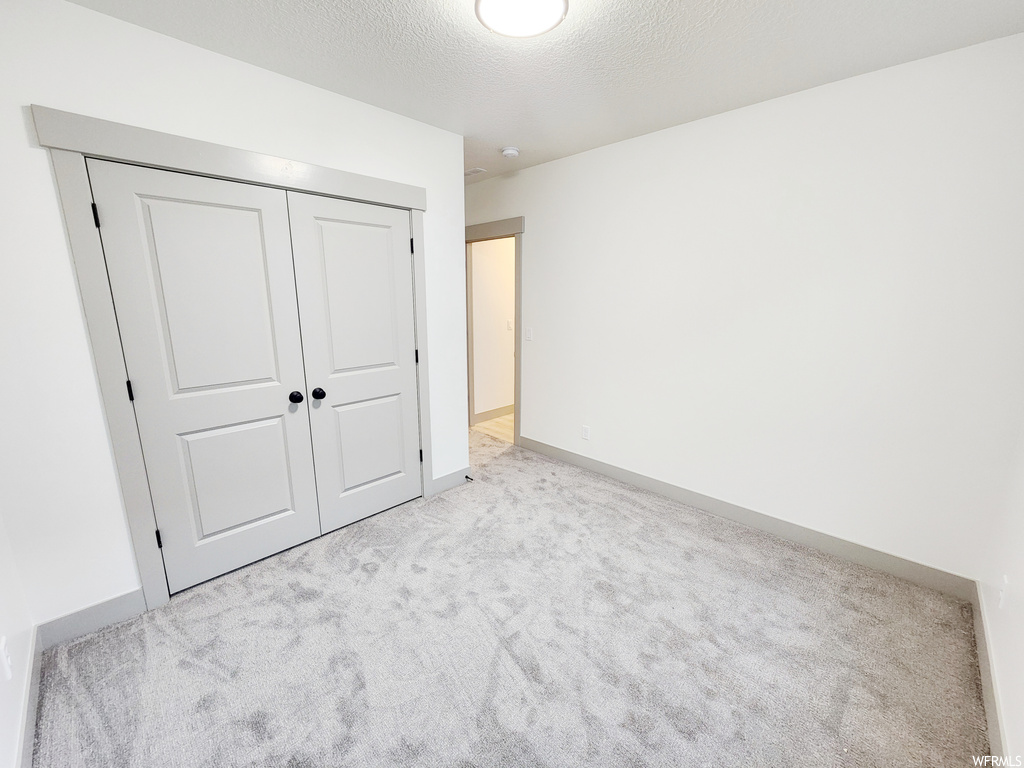 Unfurnished bedroom featuring light carpet, a closet, and a textured ceiling