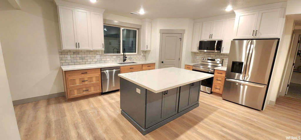 Kitchen with a kitchen island, white cabinets, light wood-type flooring, and stainless steel appliances
