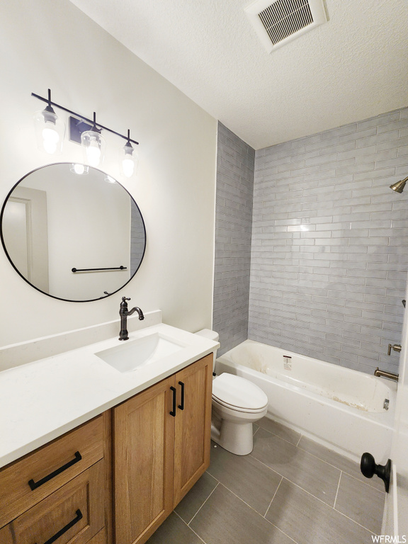 Full bathroom featuring toilet, vanity, tile flooring, tiled shower / bath, and a textured ceiling