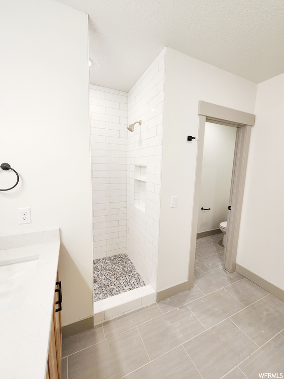 Bathroom with toilet, vanity, a tile shower, and tile flooring