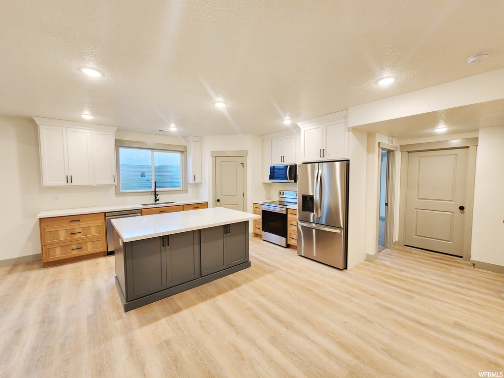 Kitchen featuring stainless steel appliances, light hardwood / wood-style floors, a center island, and white cabinetry