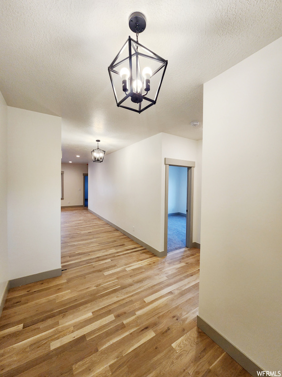 Unfurnished room featuring a chandelier, light hardwood / wood-style floors, and a textured ceiling