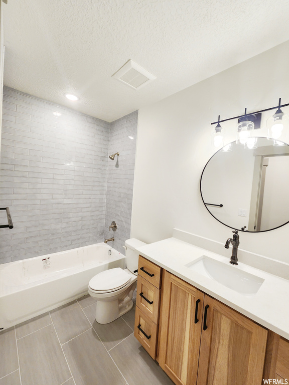 Full bathroom with vanity, tiled shower / bath, a textured ceiling, tile floors, and toilet