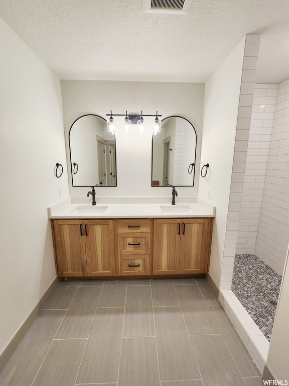 Bathroom with oversized vanity, a tile shower, and double sink