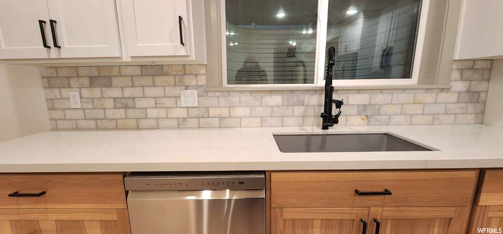 Kitchen featuring sink, white cabinets, stainless steel dishwasher, and backsplash