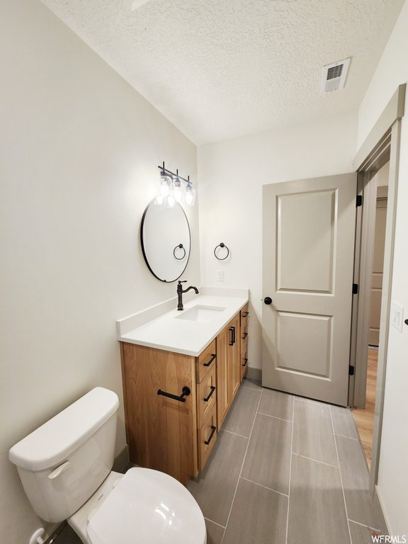 Bathroom featuring a textured ceiling, toilet, vanity, and tile flooring