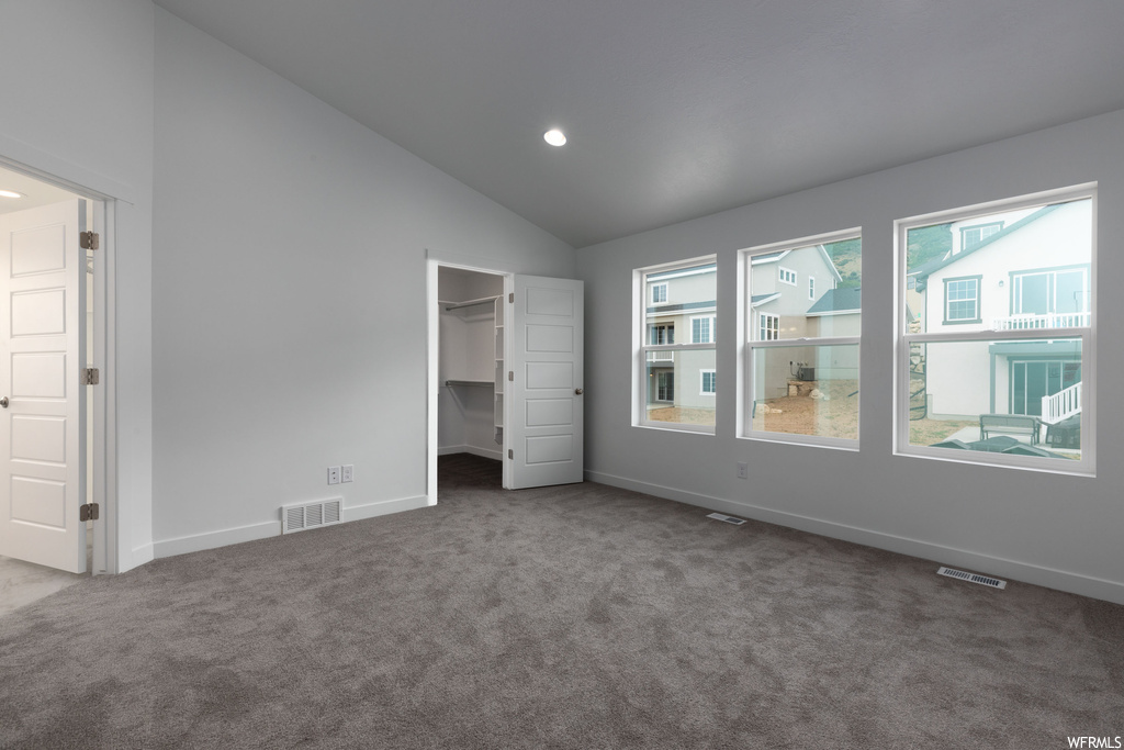 Unfurnished bedroom with a closet, lofted ceiling, a walk in closet, and dark colored carpet