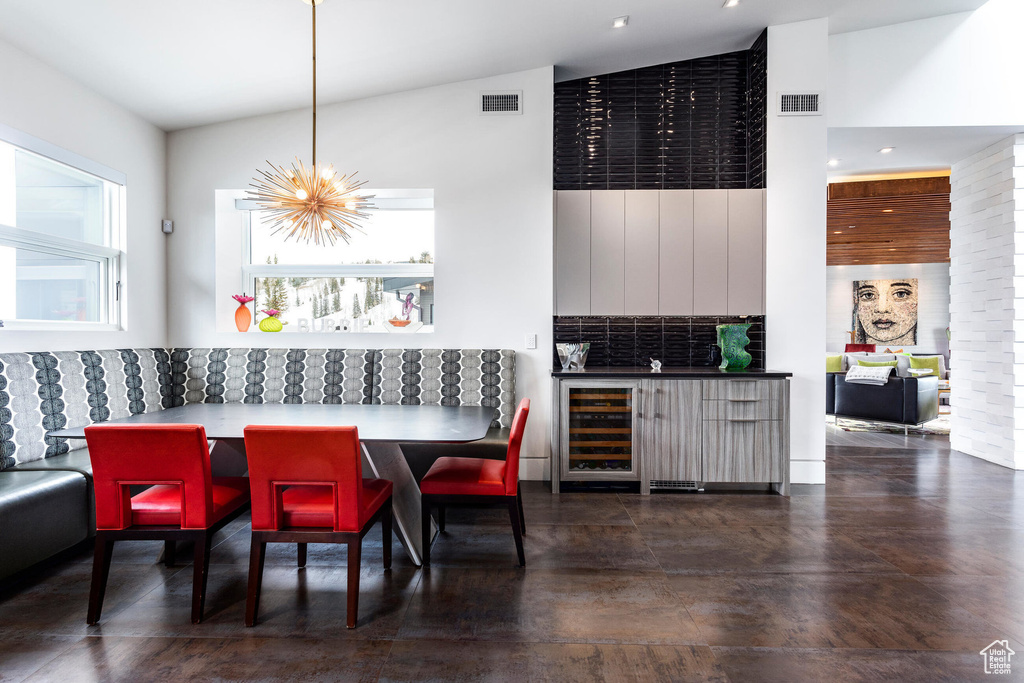 Dining space featuring a towering ceiling, wine cooler, concrete flooring, and a chandelier