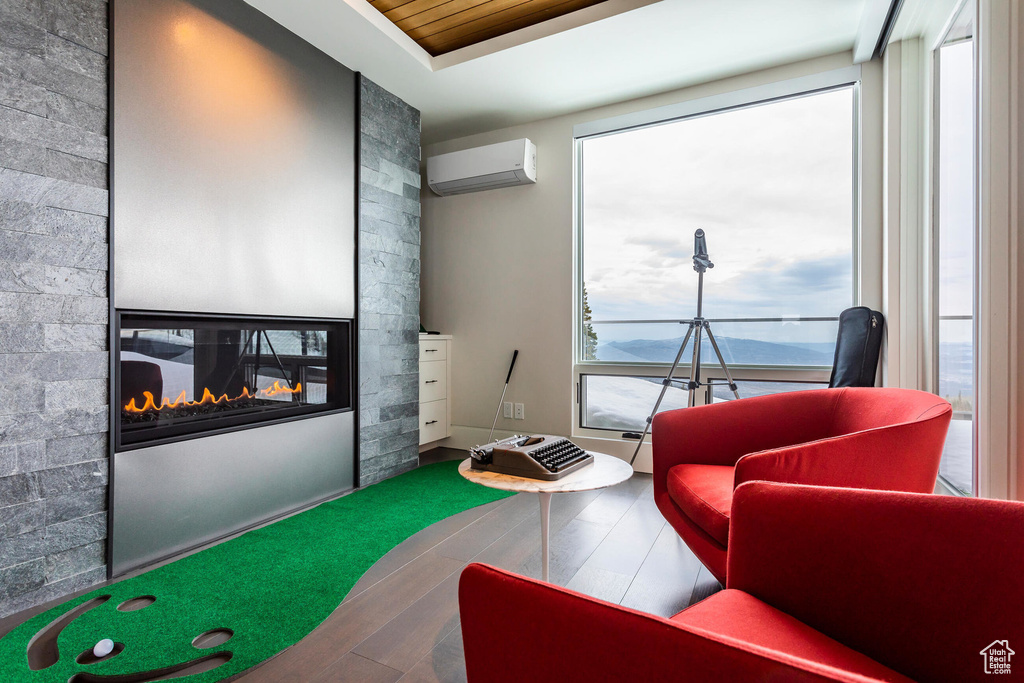 Sitting room with an AC wall unit, wood finished floors, and a multi sided fireplace