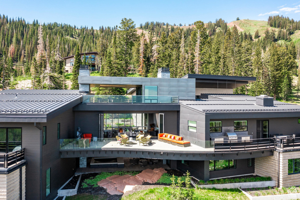 Rear view of house with a forest view, a chimney, a balcony, metal roof, and a standing seam roof