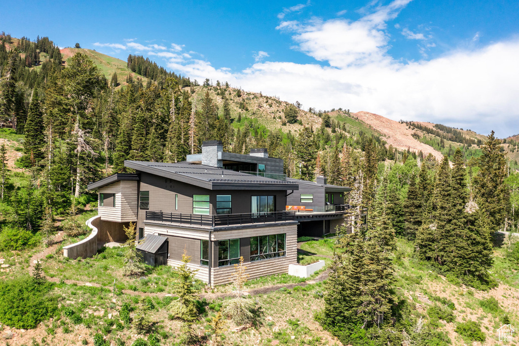 Back of house featuring a chimney, a view of trees, a mountain view, and a balcony