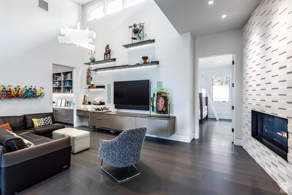 Living area with dark wood-style flooring, a tile fireplace, recessed lighting, and a towering ceiling