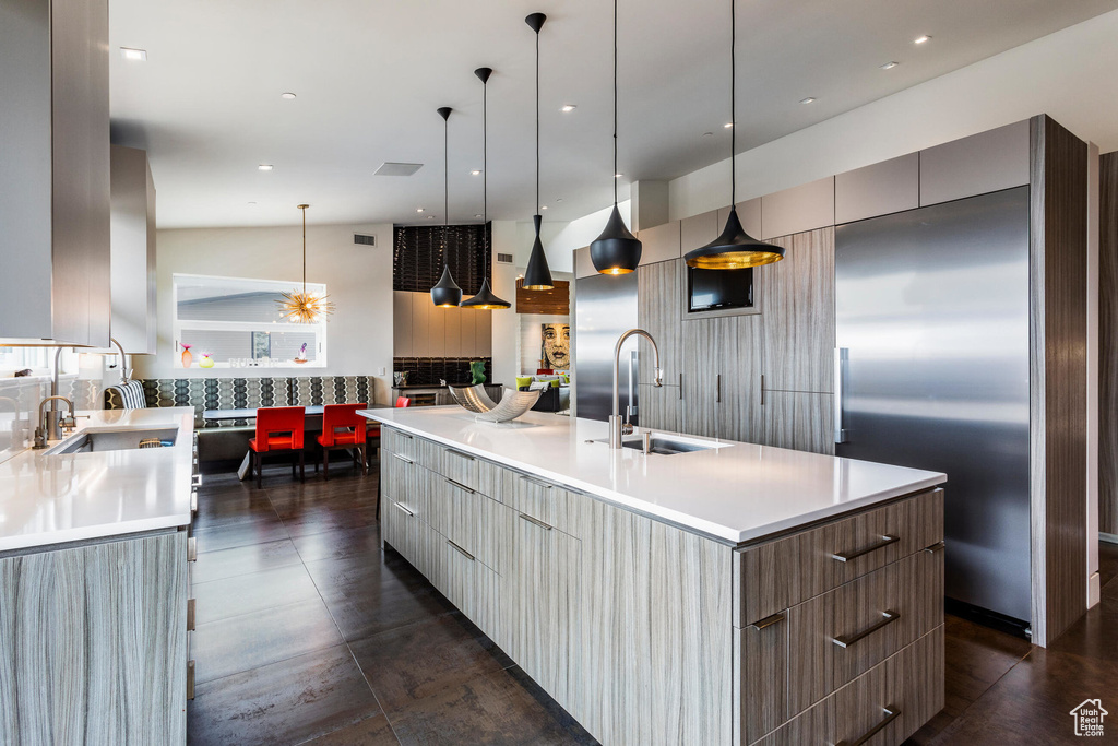 Kitchen with modern cabinets, built in refrigerator, a sink, a large island with sink, and light countertops